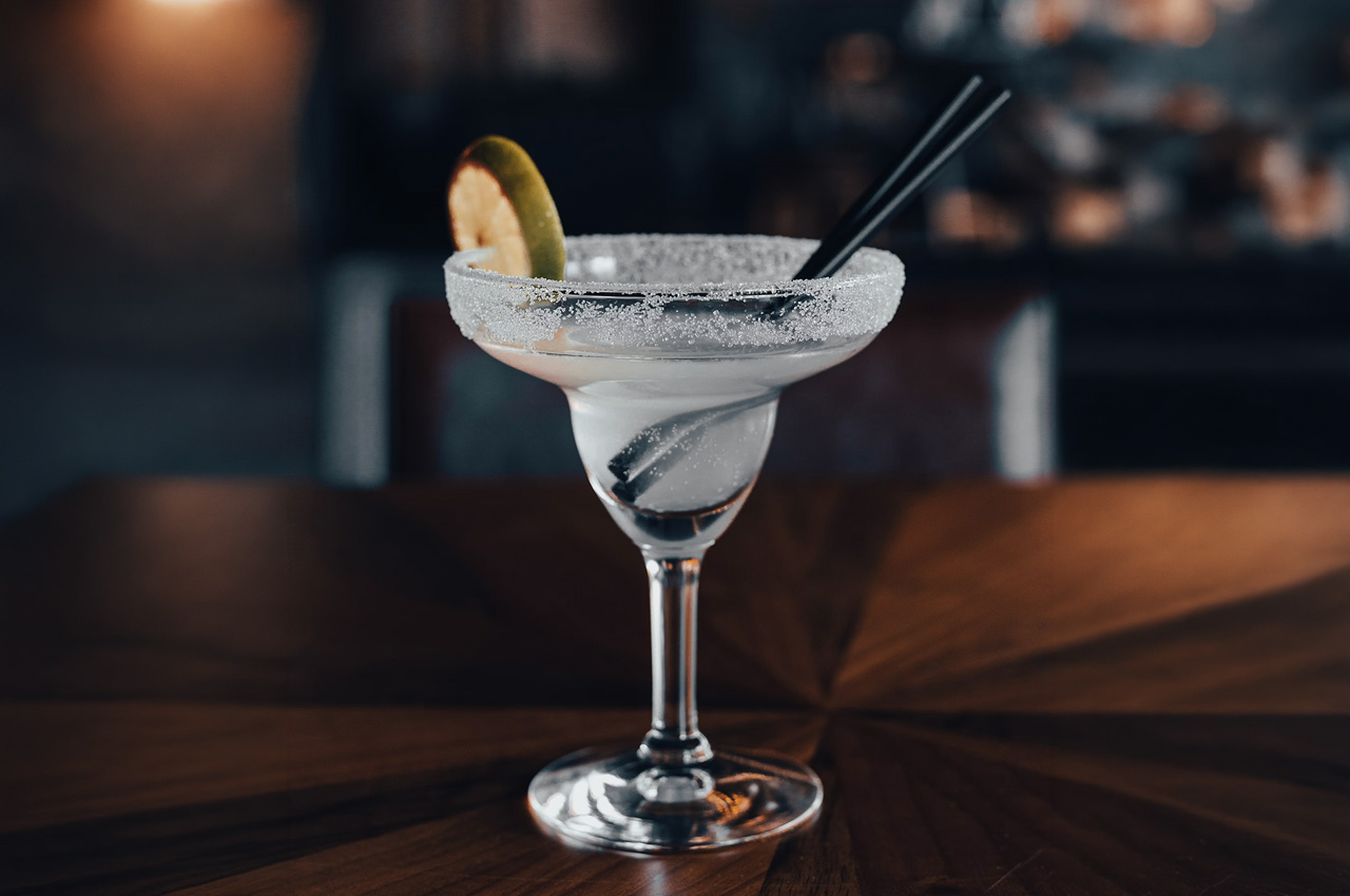 copa de margarita con borde de sal sobre fondo oscuro de bar