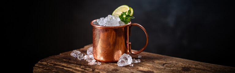 mezcal mule en taza de cobre con limón verde sobre fondo oscuro