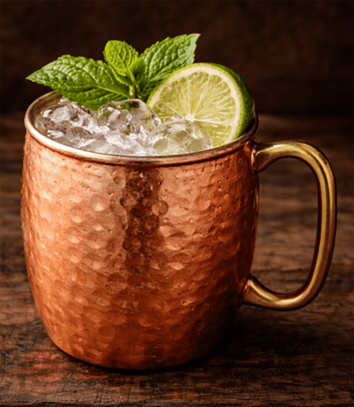 Taza de cobre con cóctel y rodaja de limón, ambiente oscuro y tenue