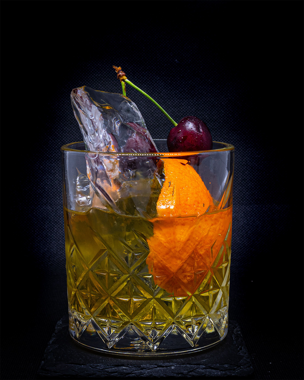 whiskey cocktail con naranja y cereza fondo oscuro